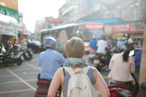 Femme blonde en marcel de dos avec un sac à dos dans une ruelle pauvre