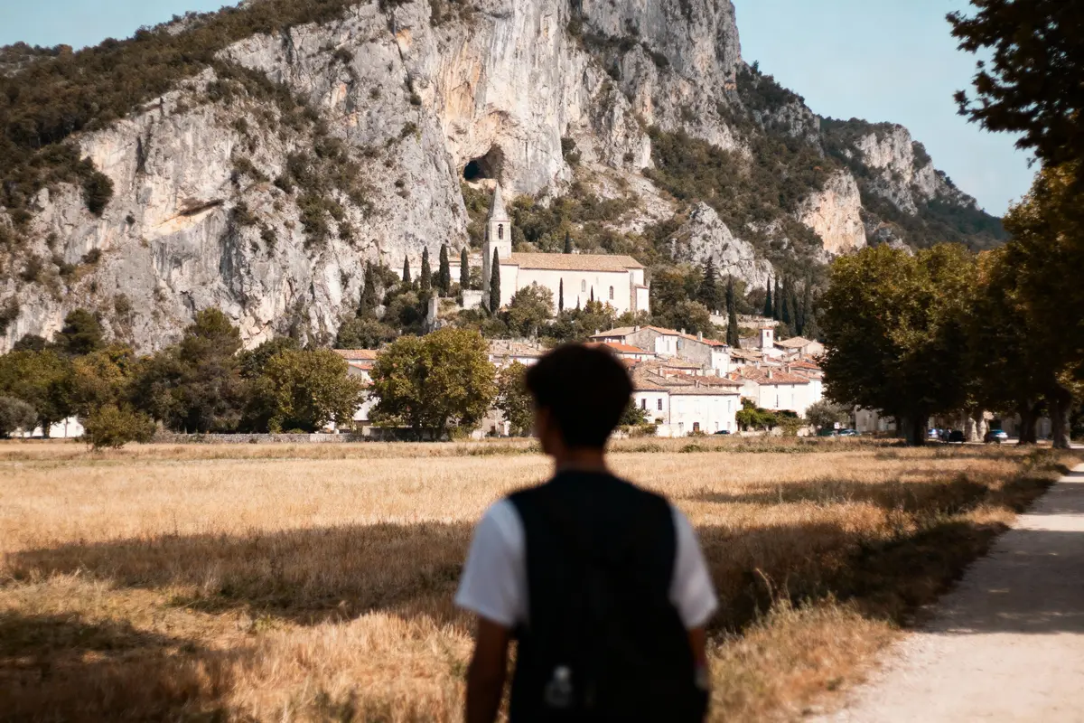 Une personne marche vers une église pittoresque entourée de montagnes et de végétation verdoyante.