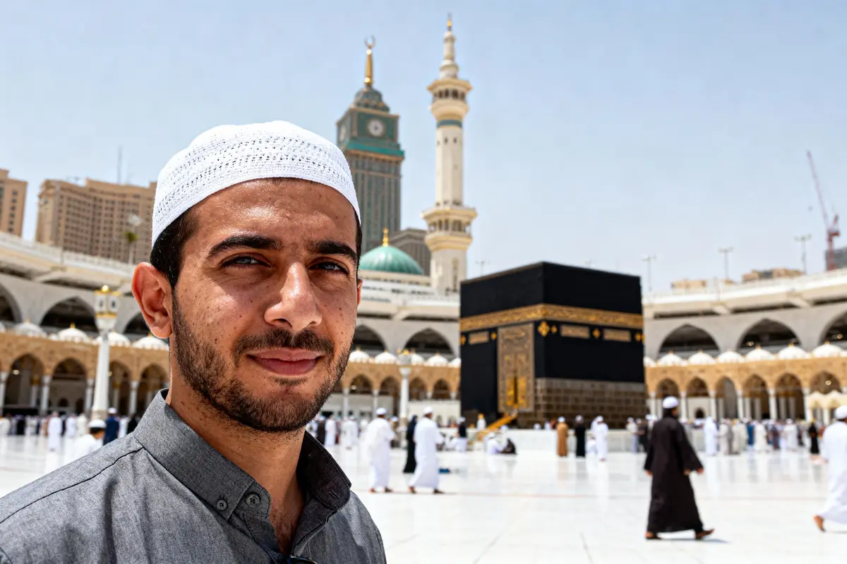 Homme en tenue traditionnelle devant la Kaaba, mosquée sacrée de La Mecque, avec minarets en arrière-plan.