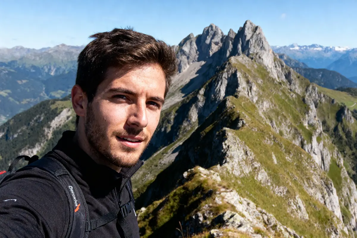 Homme prenant un selfie en montagne, paysages alpins spectaculaires en arrière-plan, ciel bleu et ensoleillé.