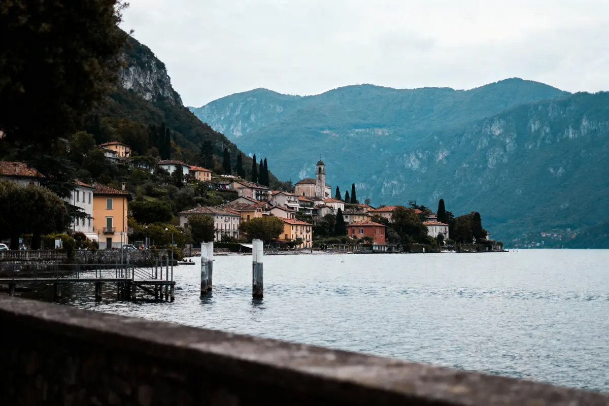 Village pittoresque au bord d'un lac, entouré de montagnes, avec maisons colorées et un clocher visible.