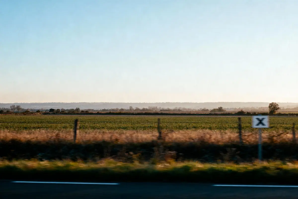 Paysage champêtre avec champs verts, ciel bleu clair, panneau "X" près de la route.