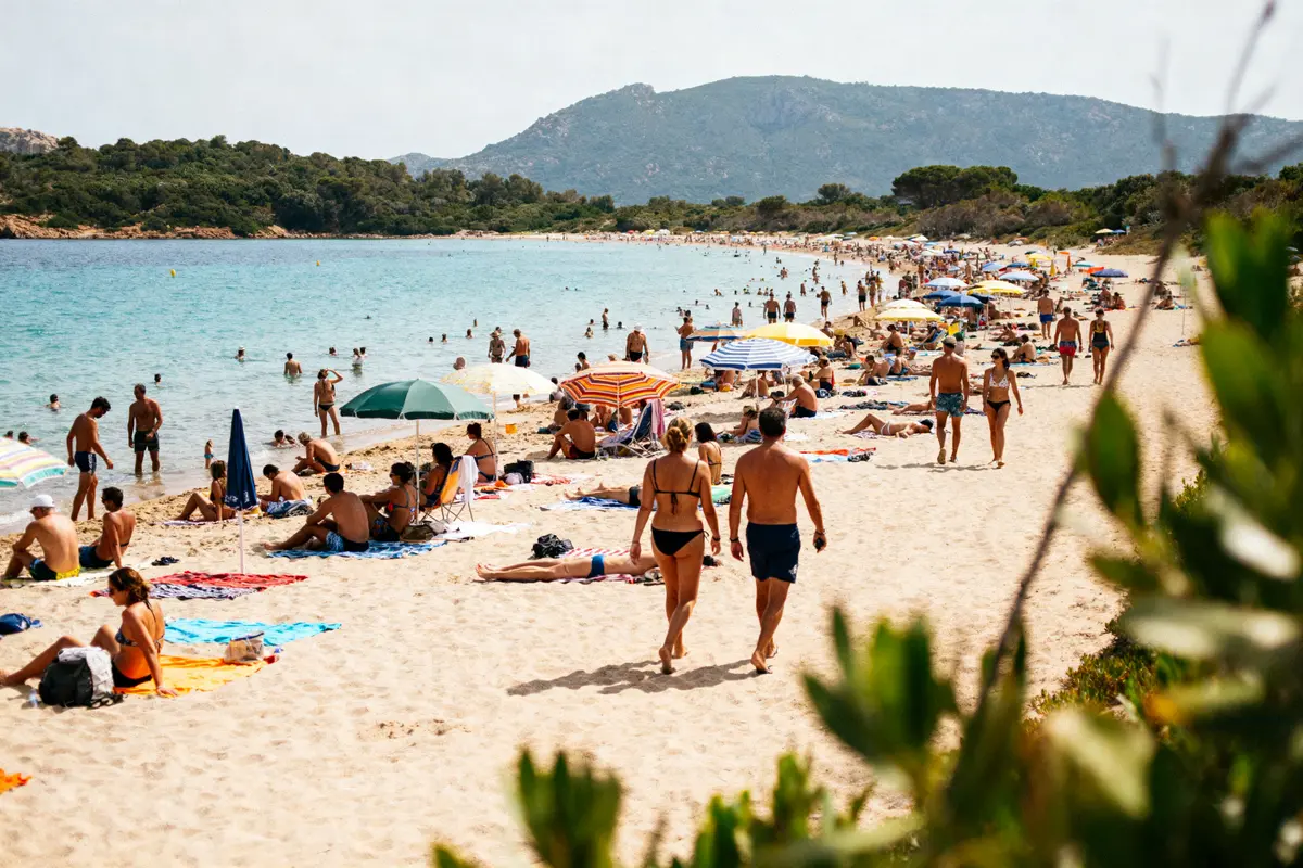 Plage ensoleillée avec baigneurs, parasols colorés et collines en arrière-plan, bordée d'arbres et mer bleue.