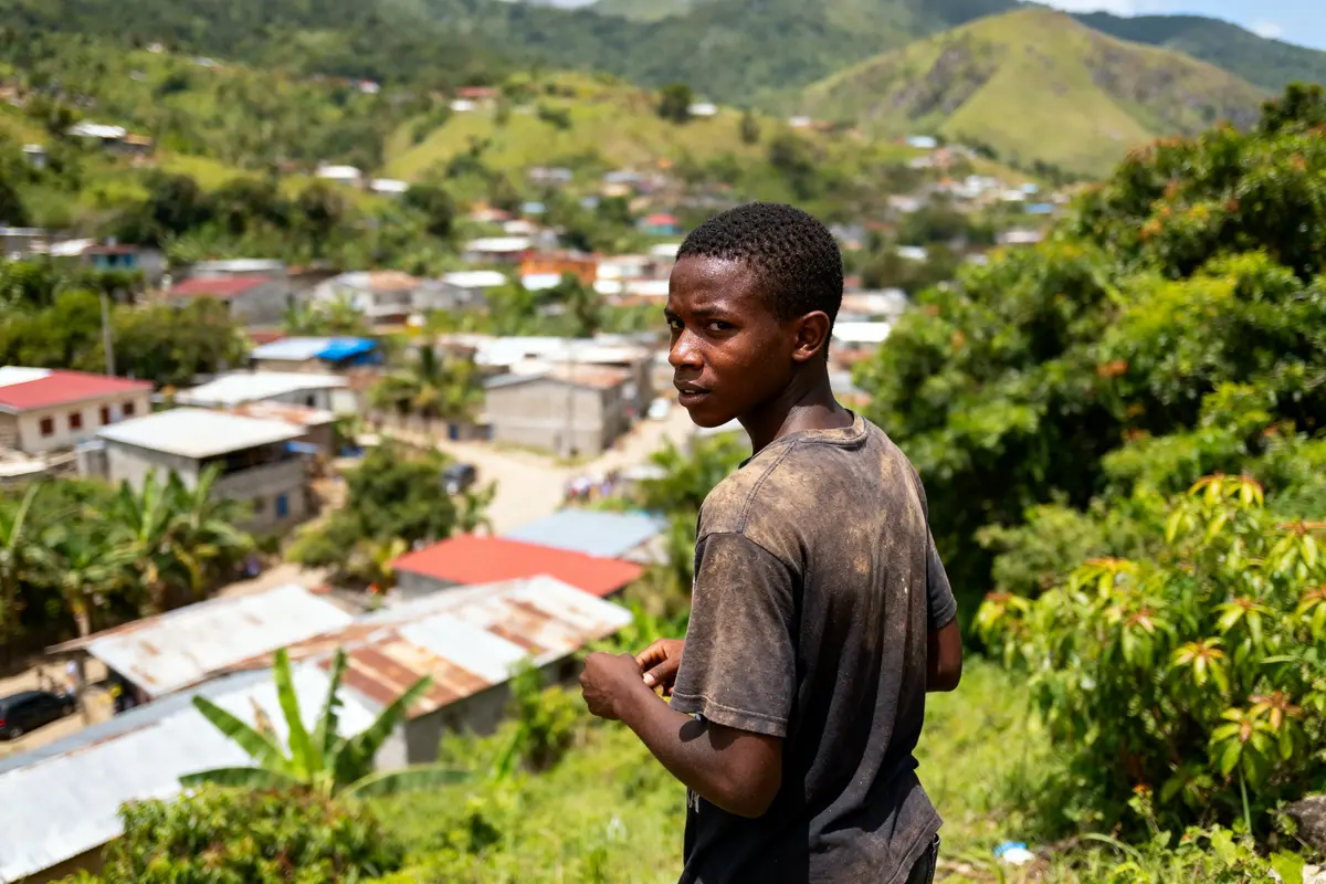 Jeune homme regardant vers l'arrière, avec un village et des collines verdoyantes en arrière-plan.