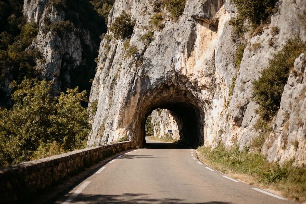 Route traversant un tunnel creusé dans une falaise rocheuse entourée de verdure, sous un ciel bleu.