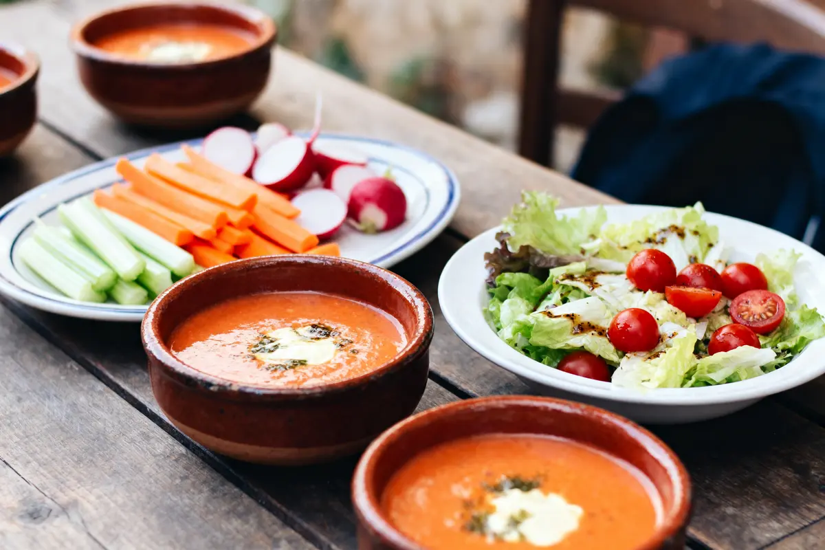 Assiette salade, soupe, légumes crus en bâtonnets, table en bois, repas sain et coloré extérieur.