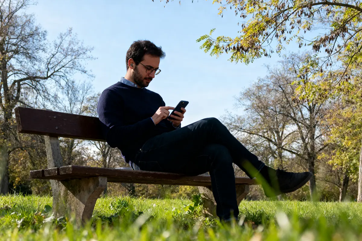 Homme assis sur un banc utilisant avis-et-notes.fr sur son téléphone dans un parc