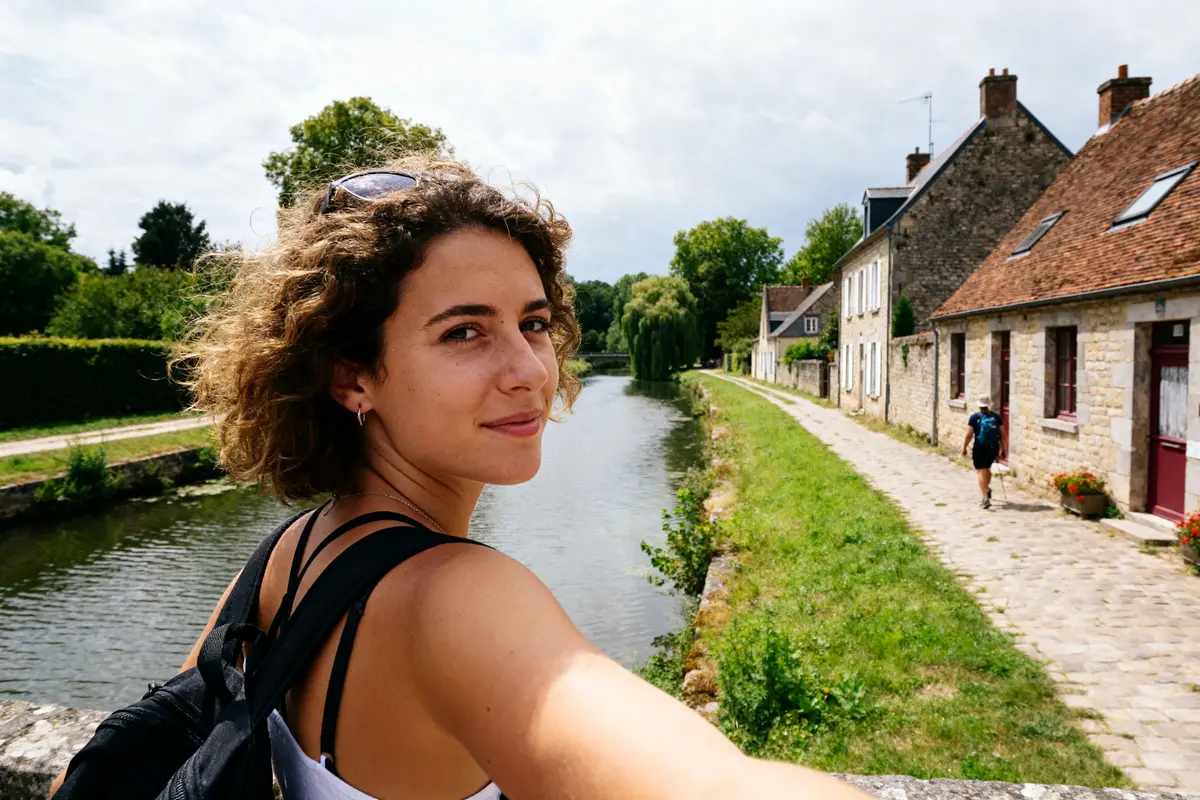 Jeune femme souriante près d'un canal pittoresque, parfaite balade morlies au calme.