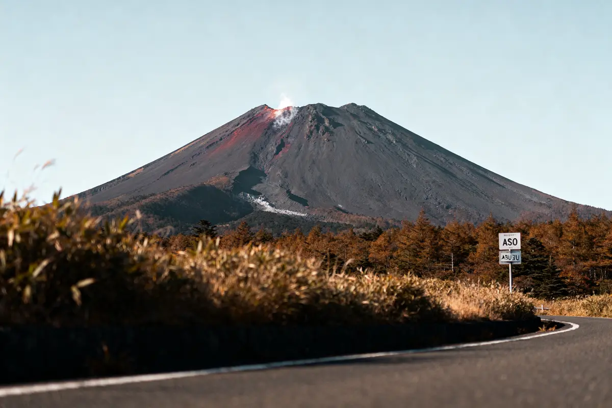 Route menant au volcan Aso du Japon avec sommet fumant en arrière-plan